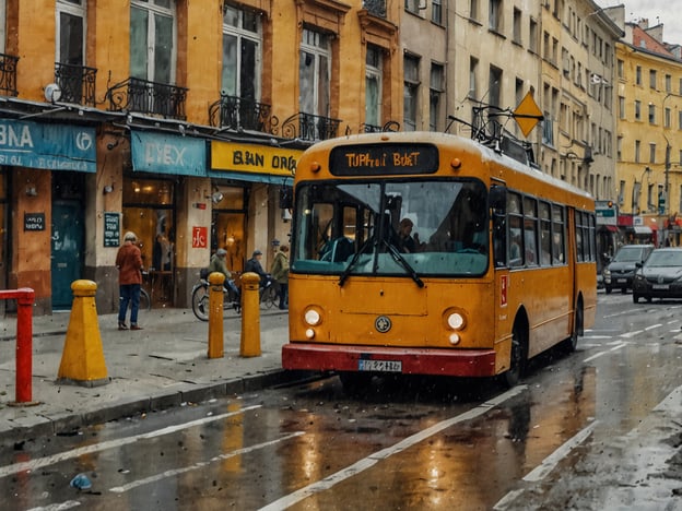 Auf dem Bild ist ein gelber Trolleybus zu sehen, der in einer Stadt fährt. Der öffentliche Verkehr wird hier durch den Trolleybus symbolisiert, der elektrisch betrieben wird und oft in städtischen Gebieten zu finden ist. Die Straße ist nass vom Regen, und es sind auch Fußgänger sowie Fahrradfahrer in der Nähe zu sehen, was ein lebendiges Bild der Fortbewegung in der Stadt vermittelt. Die Umgebung ist städtisch, mit Geschäften und Gebäuden im Hintergrund.